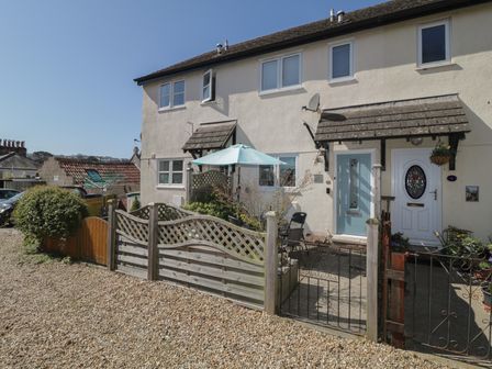 A terrace house with a gravel front garden and a blue umbrella over outdoor furniture at Malting Cottage in Dawlish