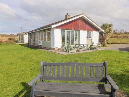 A single-story house with a patio and outdoor chairs and table in a grassy yard at Seafield in Rhydwyn near Cemaes Bay