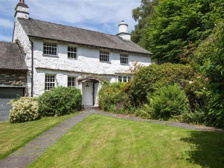 A stone cottages with a sloped roof surrounded by greenery and a stone path at The Cragg in Hawkshead