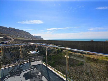 A balcony with two chairs and a table overlooking a rocky shoreline and the sea at Sunset Lodge in Fortuneswell