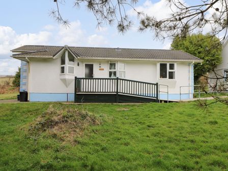A white single-story house with a gray tiled roof and a ramp in front surrounded by grass at Nanny Jill's Cabin in Tegryn near Crymych
