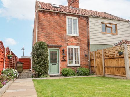A brick house with a green door and garden surrounded by wooden fences at 1 Rumsby Cottages in Gisleham near Kessingland