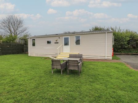 An exterior view of a beige caravan with a white door a set of steps and outdoor table with chairs on grass at Caravan in Llangefni