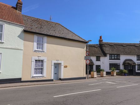 A street with two houses one with a tiled roof and the other with a thatched roof and a bollard with traffic signs at Milton Cottage in Lyme Regis