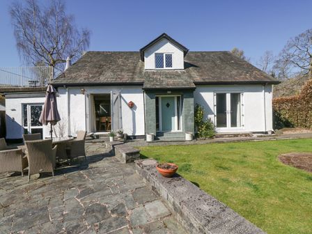 An outdoor patio with chairs and umbrella next to a white house with a sloped roof at Osprey Cottage in Grasmere