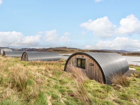 A row of curved metal and wooden cabins near water with hills in the background at Scarba in Cullipool Isle Of Luing