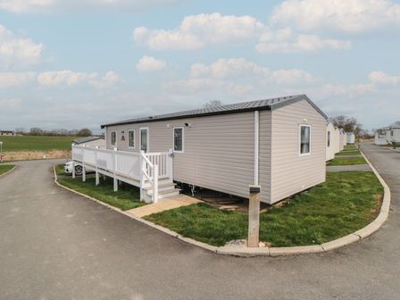 A mobile home with a white railing and steps on a corner lot in a residential area with other similar homes at Meadow View in West Thirston Felton