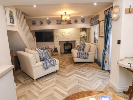 A living room with two beige sofas and blue patterned throws near a stone fireplace at 6 Uppergate Street Rose Cottage in Conwy