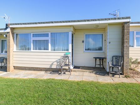 A single story exterior of a property with two chairs and a table on a paved patio at Chalet 37 in Hemsby
