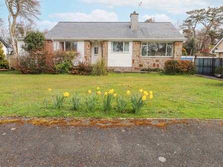 A stone and white house with a chimney fronted by a lawn with yellow flowers at 3 Glyn Y Mor in Llanbedrog