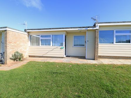 Exterior view of a single-story house with windows a door paved walkway and grass at Chalet 38 in Hemsby
