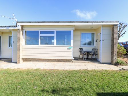 A bungalow exterior with a large window a small patio table and chairs and adjacent doors at Chalet 39 in Hemsby