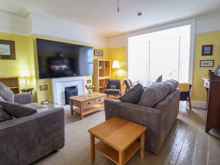 A living room with sofas a large wall mounted television and wooden tables at Beach Haven in Aberystwyth