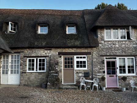 An outdoor view of a cottage with a thatched roof and stone wall at Bracken Cottage in