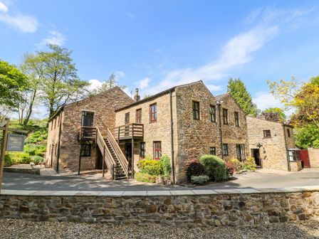 Stone building with wooden stairs and landscaping under blue sky at Wolfen Mill in Chipping