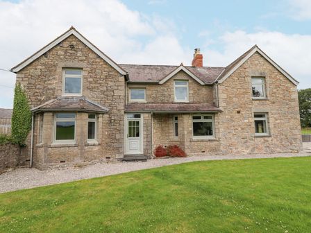 A stone house with multiple windows a white front door and green grass in front at Segrwyd Uchaf in Denbigh near Conwy