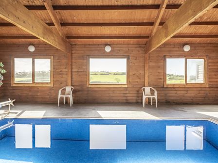 An indoor pool area with large windows and chairs at Cove Cottage Llangrannog