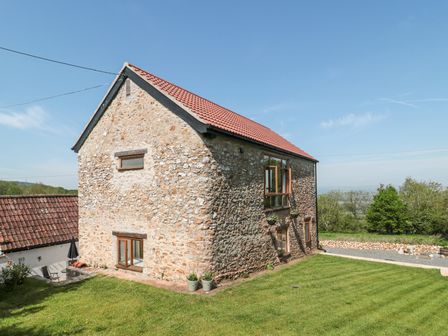 A stone house with a tiled roof and multiple windows on a grass lawn surrounded by trees at Newlands Barn in Wellington