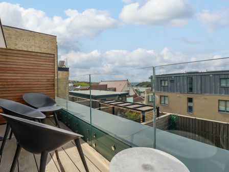 A balcony with three black chairs and a round table overlooking buildings and the sea at Ebbtide in Newquay