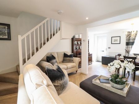 A living room with beige sofas black pillows a staircase and a dining area at 3 Rosemary Lane Conwy