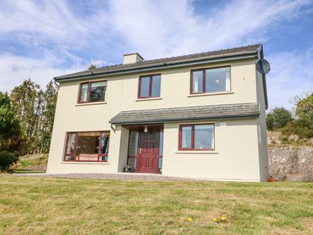 A two story house with multiple windows and a front door on a grassy lawn at Teach Ards in Kilgarvan County Kerry