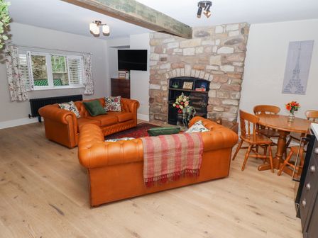 A living room with two orange sofas a stone fireplace and a wooden dining table with chairs at Muffins in Wooler