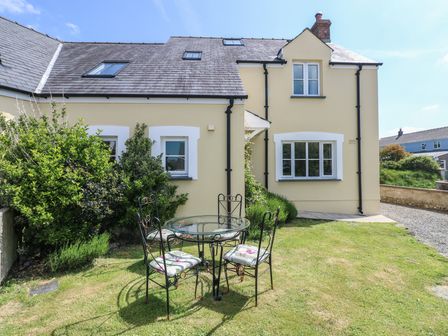 A yellow house with white window frames a glass table and four chairs on a lawn at 5 Cart-Tws Bach in St Davids