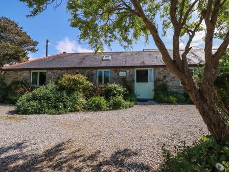 A stone cottage with green doors and windows surrounded by plants and trees at The Old Piggery in Porthtowan