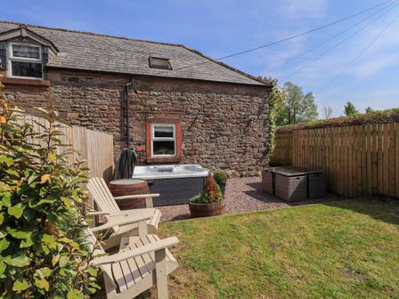 A garden area with wooden chairs a hot tub and a stone building at Corner Cottage in Unthank near Penrith