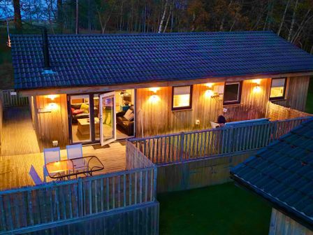 A house with a deck and chairs at Woodburn Lodge in Otterburn