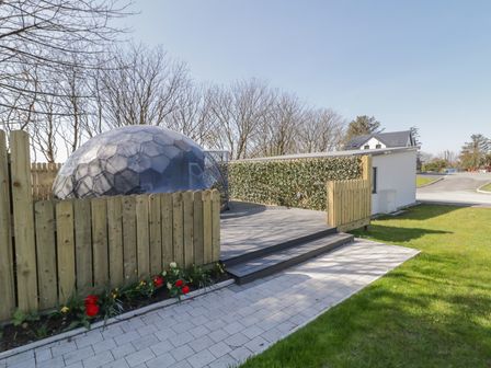 An outdoor area with a wooden fence, a walkway, flowers, a dome structure, and a building at Number 1 Dome in Derrybeg County Donegal