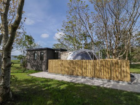 A small building with a transparent geodesic dome and a wooden fence surrounded by trees and grass at Number 2 Dome in Derrybeg County Donegal
