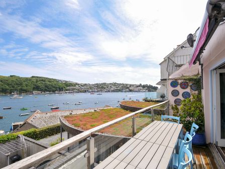 A balcony with a table and blue chairs overlooking a body of water with boats and a hillside town at 5 Esplanade in Fowey