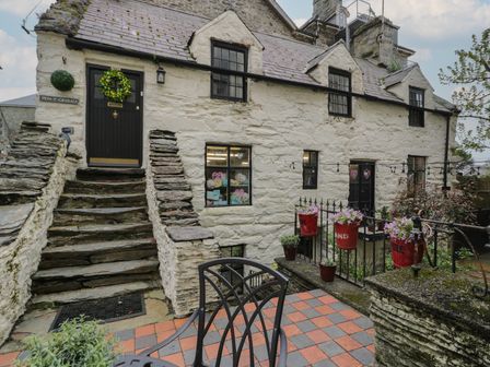 An exterior view of a stone house with stairs leading to a black door and a patio with flower pots at Pen-y-Grisiau in Barmouth