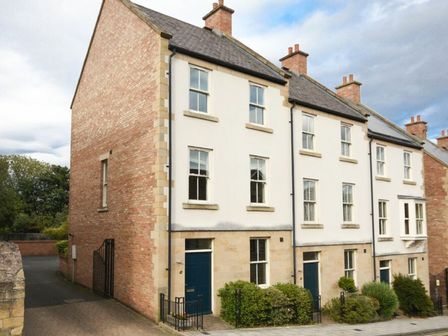 A row of brick and stone townhouses with blue doors and shrubs in front at Churchside in Alnwick