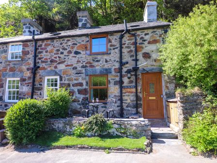 A stone cottage with a wooden door two windows and a small patio with two metal chairs and a table at 4 Old Tanrhiw in Beddgelert