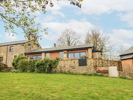 A stone house with wooden accents on a grassy hill with trees in the background at The Barn in Riding Mill near Corbridge