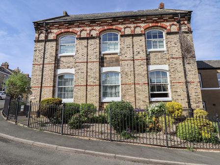 A brick building with arched windows and a small garden with bushes behind a black metal fence at Flat 2 The Old Chapel in Whitby