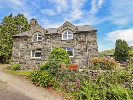 An exterior view of a stone house with diamond-pane windows and a garden with plants and shrubs at Dwynant in Bontddu near Dolgellau