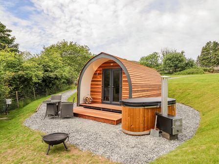 A wooden pod with glass doors next to a hot tub and outdoor furniture at Briallen in Bontddu near Dolgellau