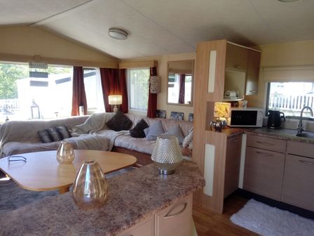 A living room with a corner sofa and pillows beside a kitchen with cabinets and appliances at Swaledale 5 Tosside near Long Preston