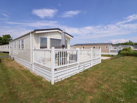 A beige static caravan with white railing and outdoor furniture on grass at Lawi39 in Towyn