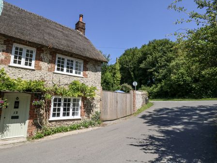 A cottage with a thatched roof and a garden at Happiness Cottage in Piddlehinton