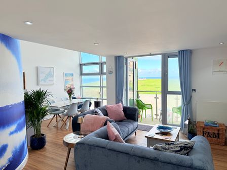 A living room with a sofa, dining table, and large windows at Penthouse @46Zinc - Headland View, Newquay