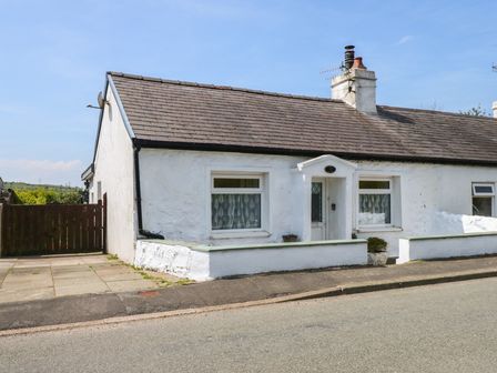 A white single-story cottage with a tiled roof and small front wall along a street at Cobweb Cottage in Waunfawr