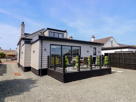 A single story house with a small deck and outdoor furniture surrounded by gravel at Bronallt in Cemaes Bay
