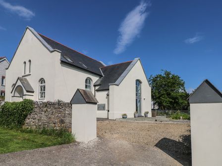 A white chapel building with a slate roof and arched windows surrounded by a low stone wall and open driveway at Zoar Chapel in Carew