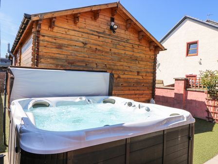 An outdoor hot tub with bubbling water next to a wooden cabin and a fenced yard at Smiddy Bothy in Edzell