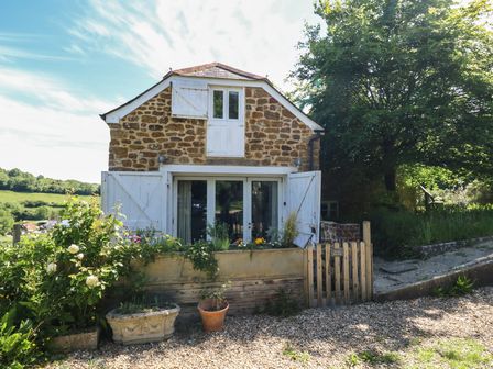 A stone house with white wooden doors and window shutters with flower pots and plants outside at The Old Flax Shop in Bridport