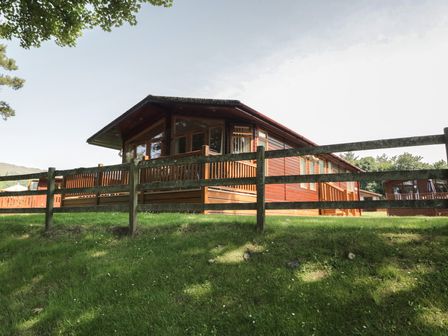 A log cabin with a wooden fence and grass at Wally's Folly, Limefitt Park near Troutbeck